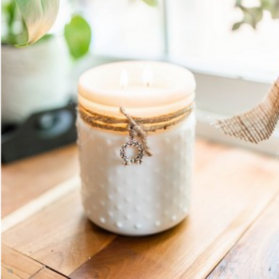 white hobnail glass jar candle with a charm on a table